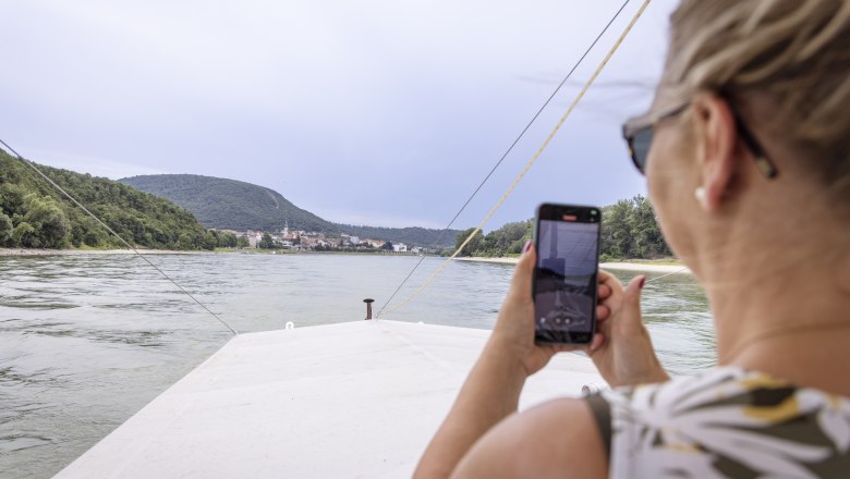 Woman on a boat takes a photo of the Danube with her cell phone.