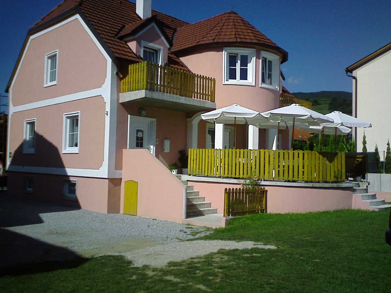 A pink guest house with terrace and parasols.