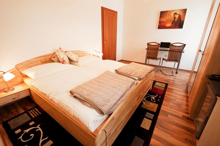 A cozy double room with wooden floor, double bed, desk and chairs.