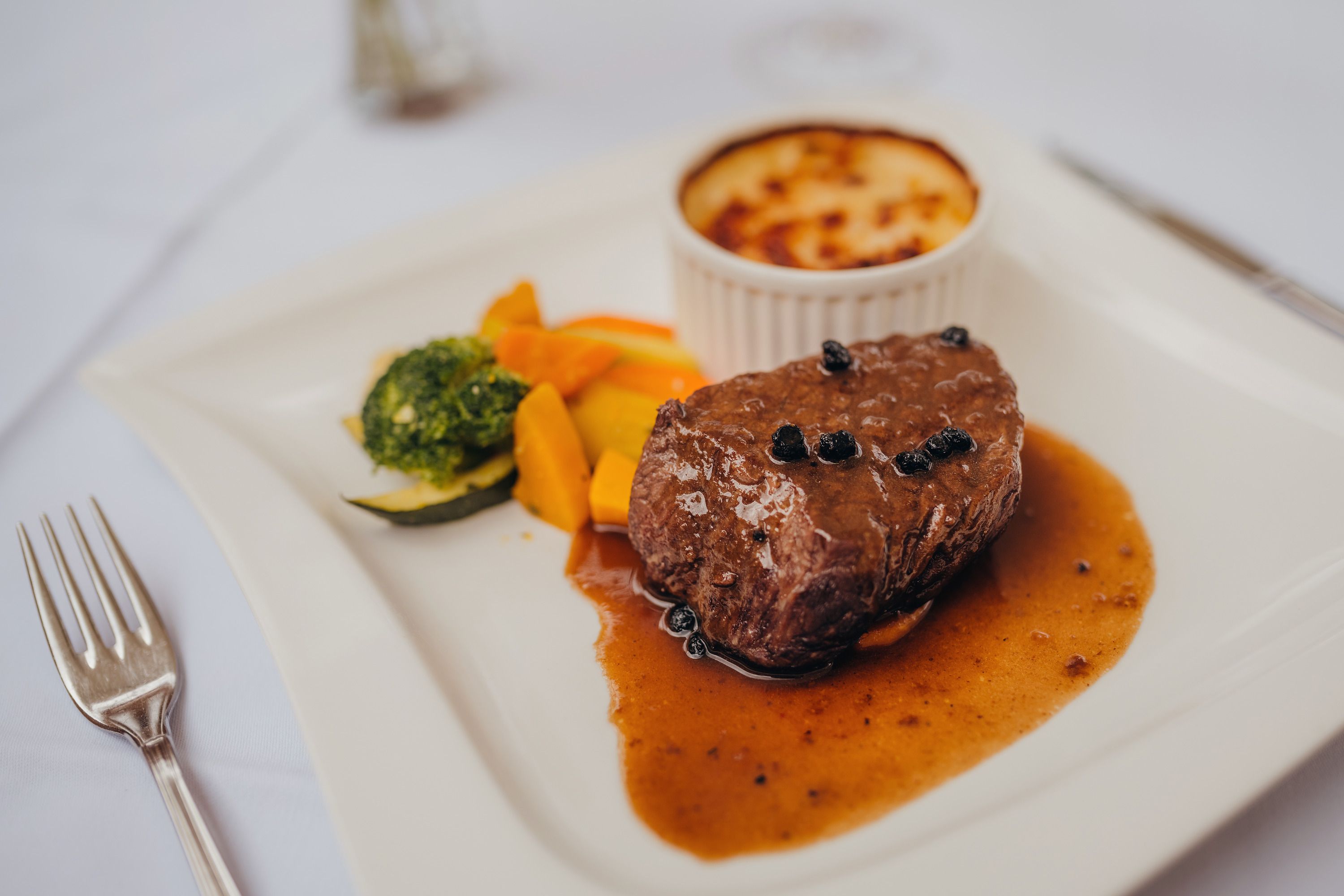 A pepper steak with sauce, vegetables and potato gratin on a white plate.