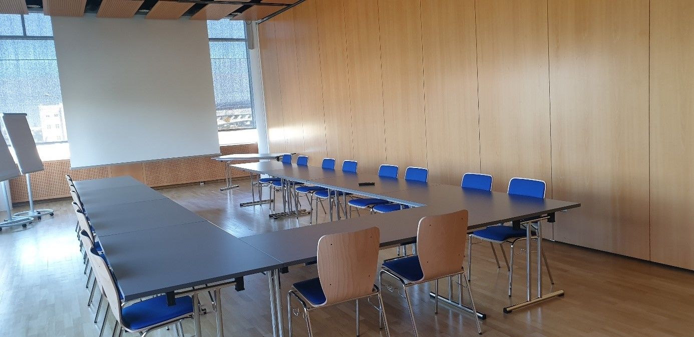 An empty conference room with U-shaped tables and blue chairs.
