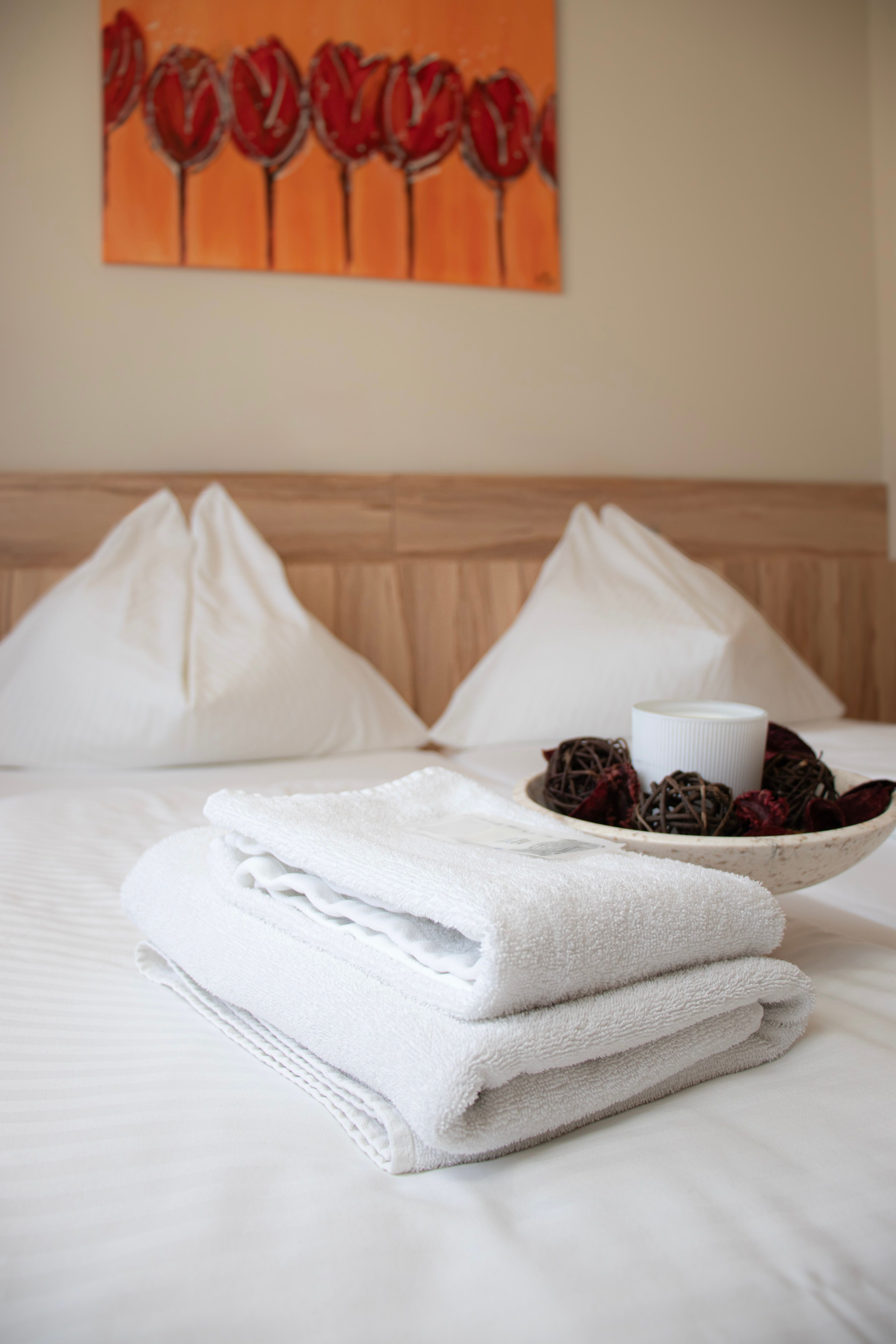 A hotel room at the Kolpinghaus with a freshly made bed, white towels, and a decorative bowl on the bed.