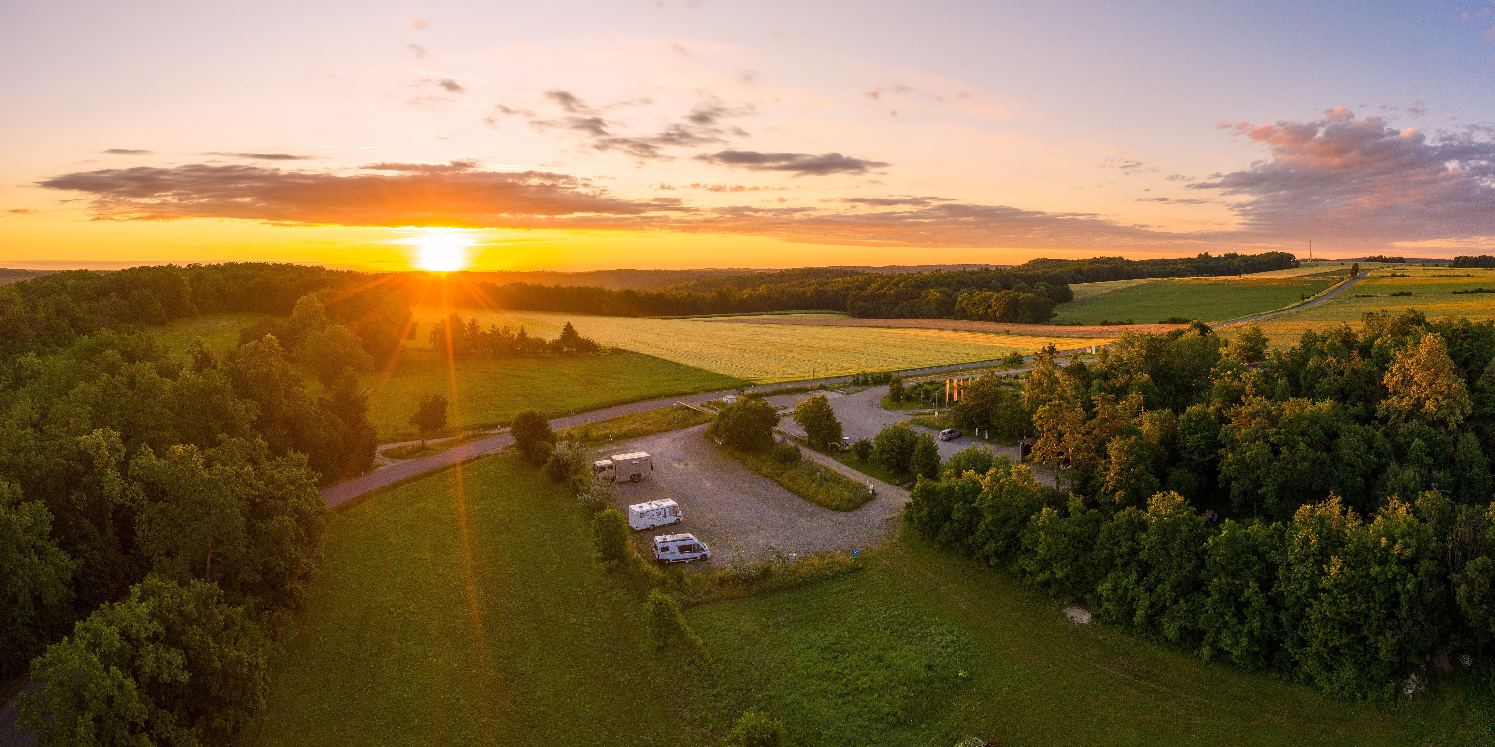 Aerial view of a motorhome site at sunset, surrounded by fields and woods.