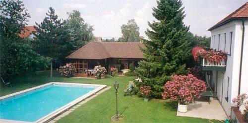 A well-kept garden with pool, trees and a house with balcony.