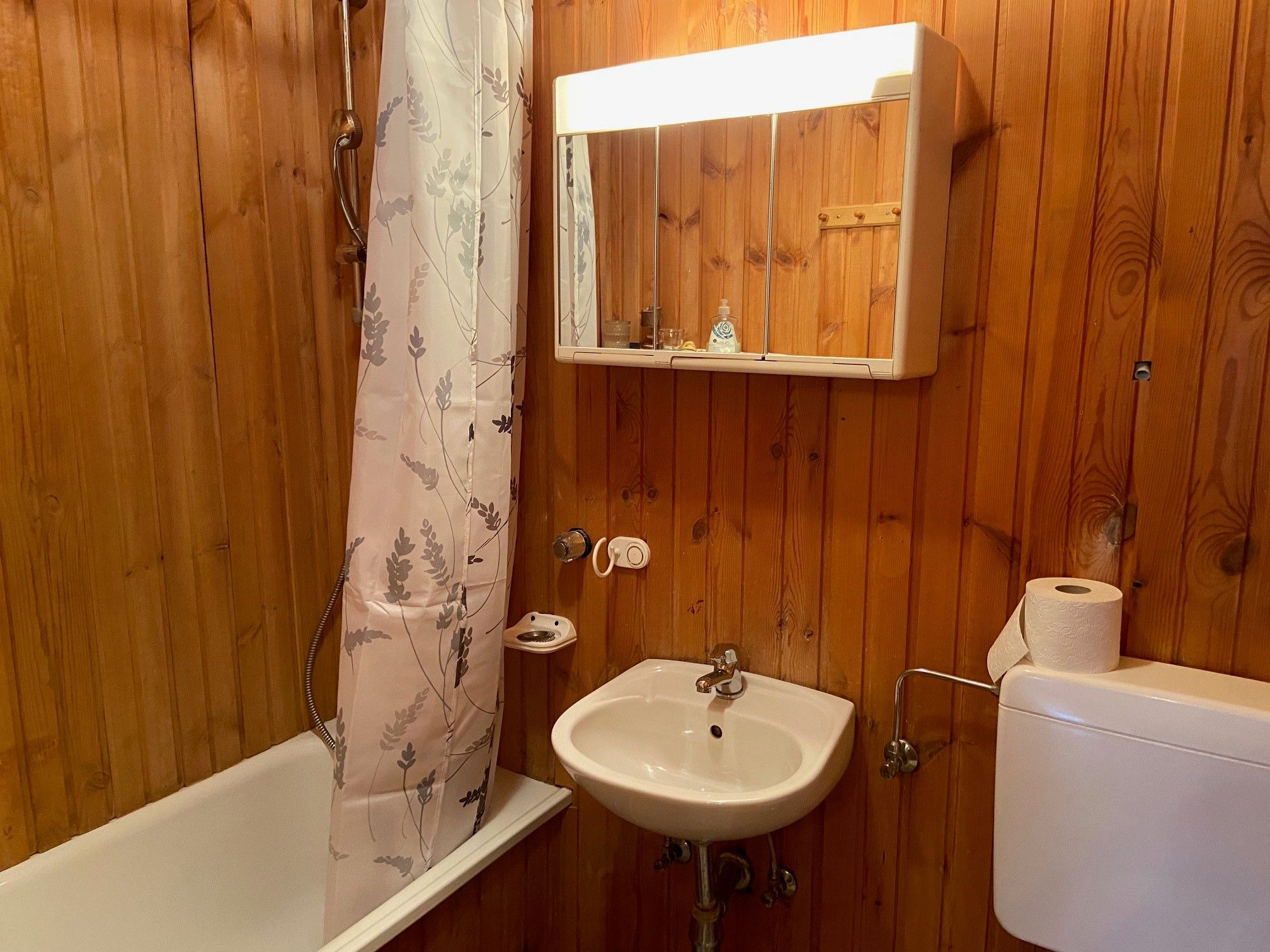 Wood-paneled bathroom with bathtub, shower curtain, washbasin and mirror cabinet.