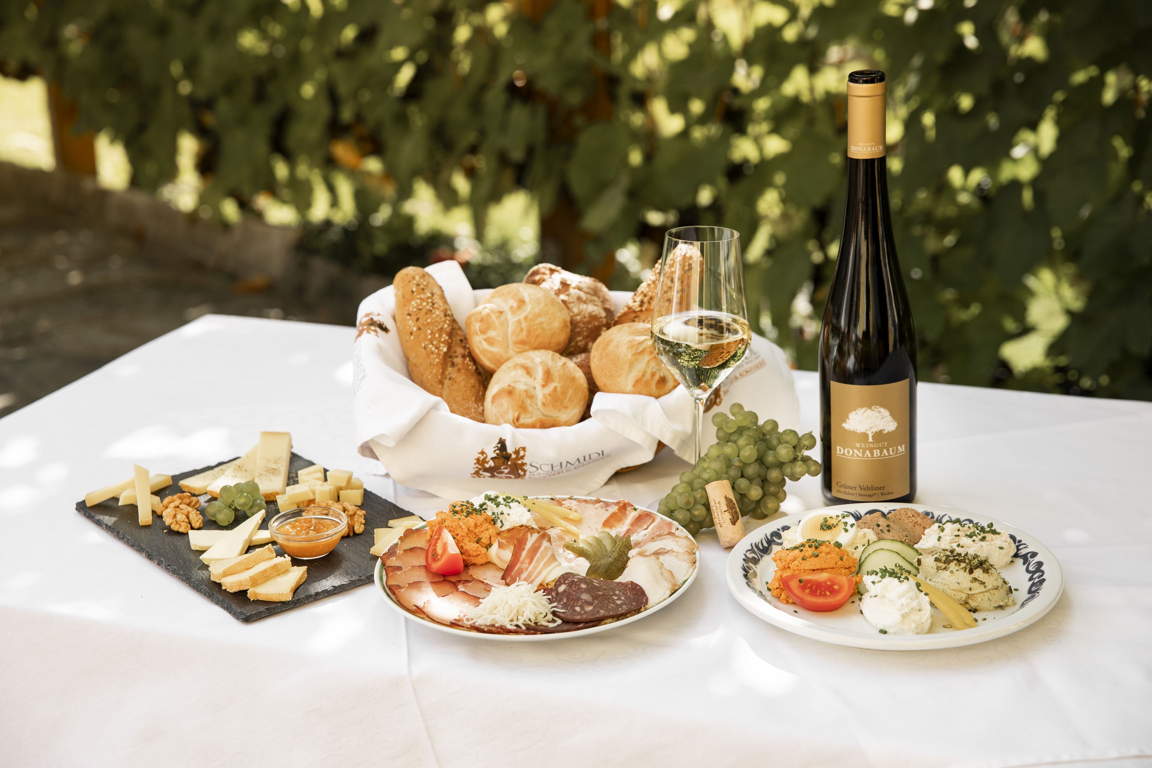 Heurigen snack with bread, cheese, cold cuts, wine and grapes on a table.