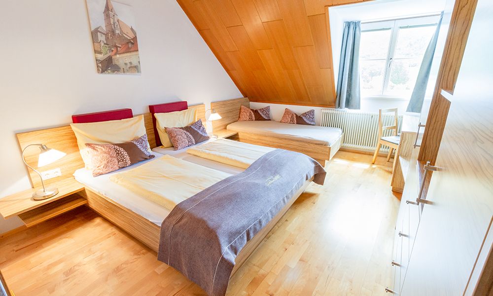 Cozy guest room with double bed, single bed, wood paneling and large window.