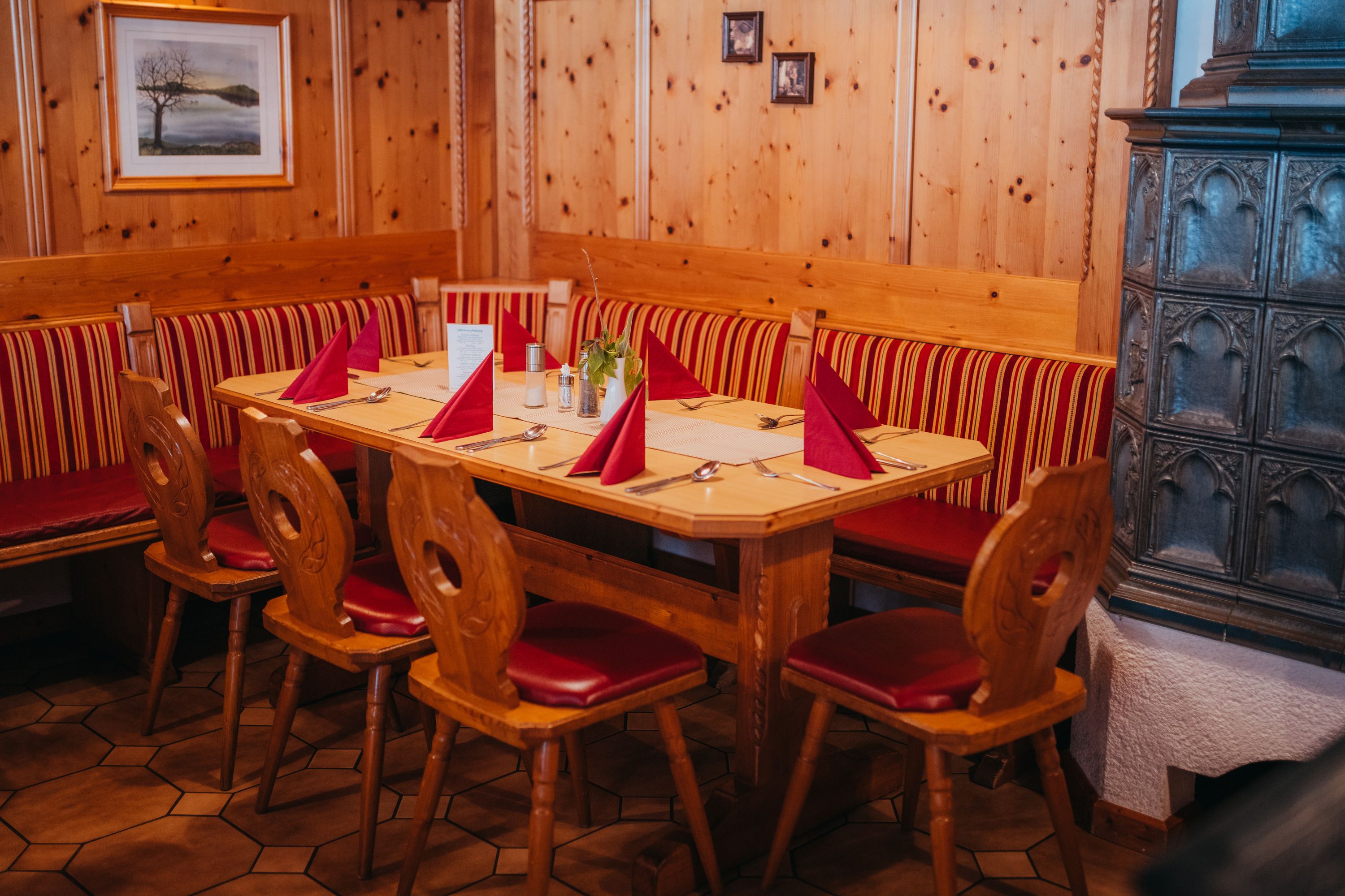 Cozy parlor with wooden furniture, red upholstery and tiled stove.