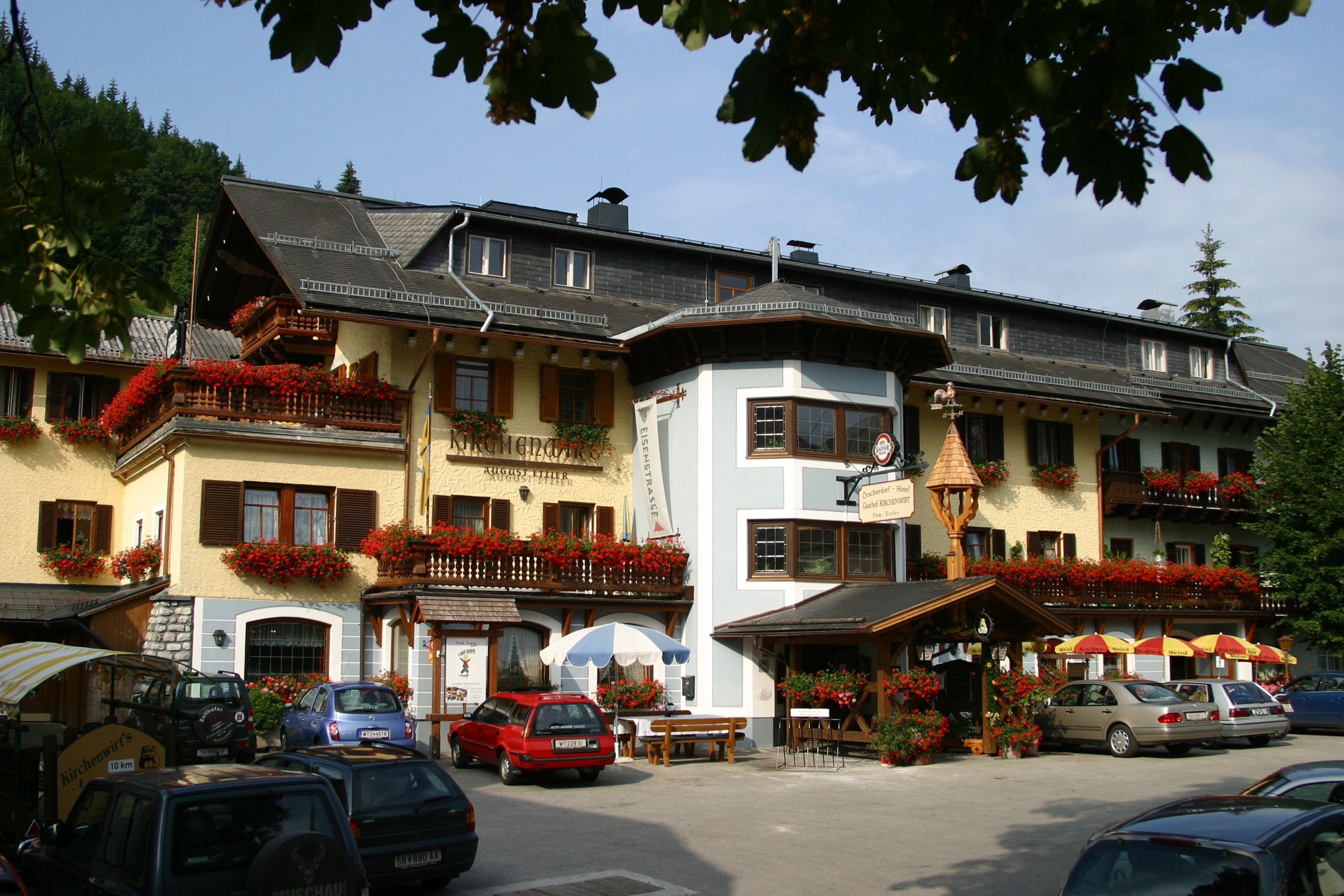 A traditional inn with flower-decorated balconies and parked cars in front of it.