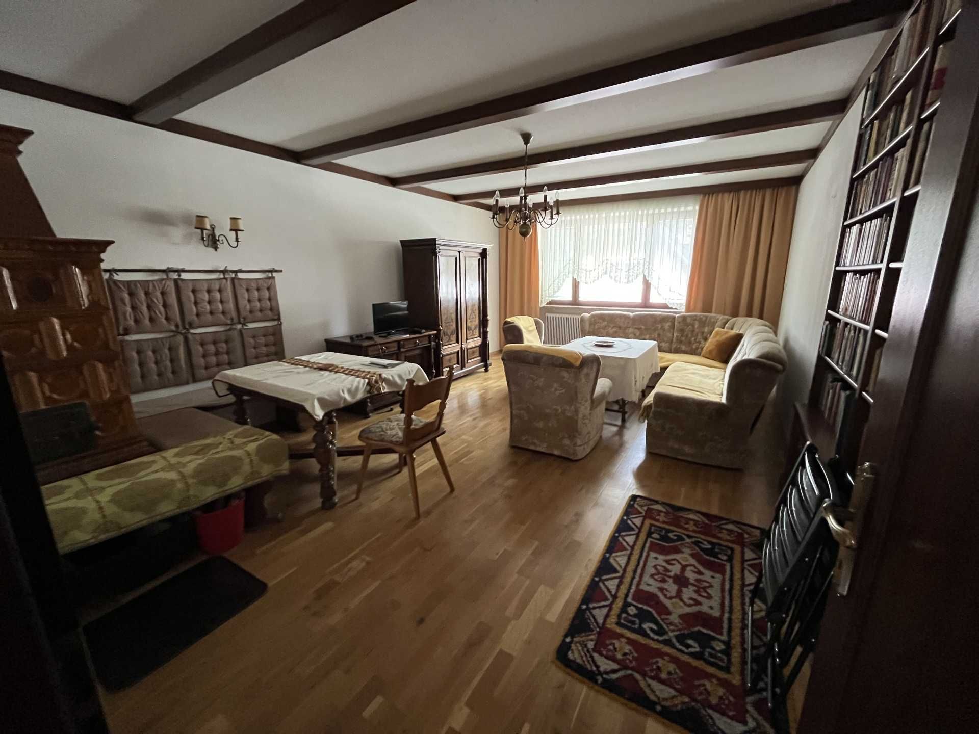 Living room with wooden floor, sofa, table, cupboard and fireplace.