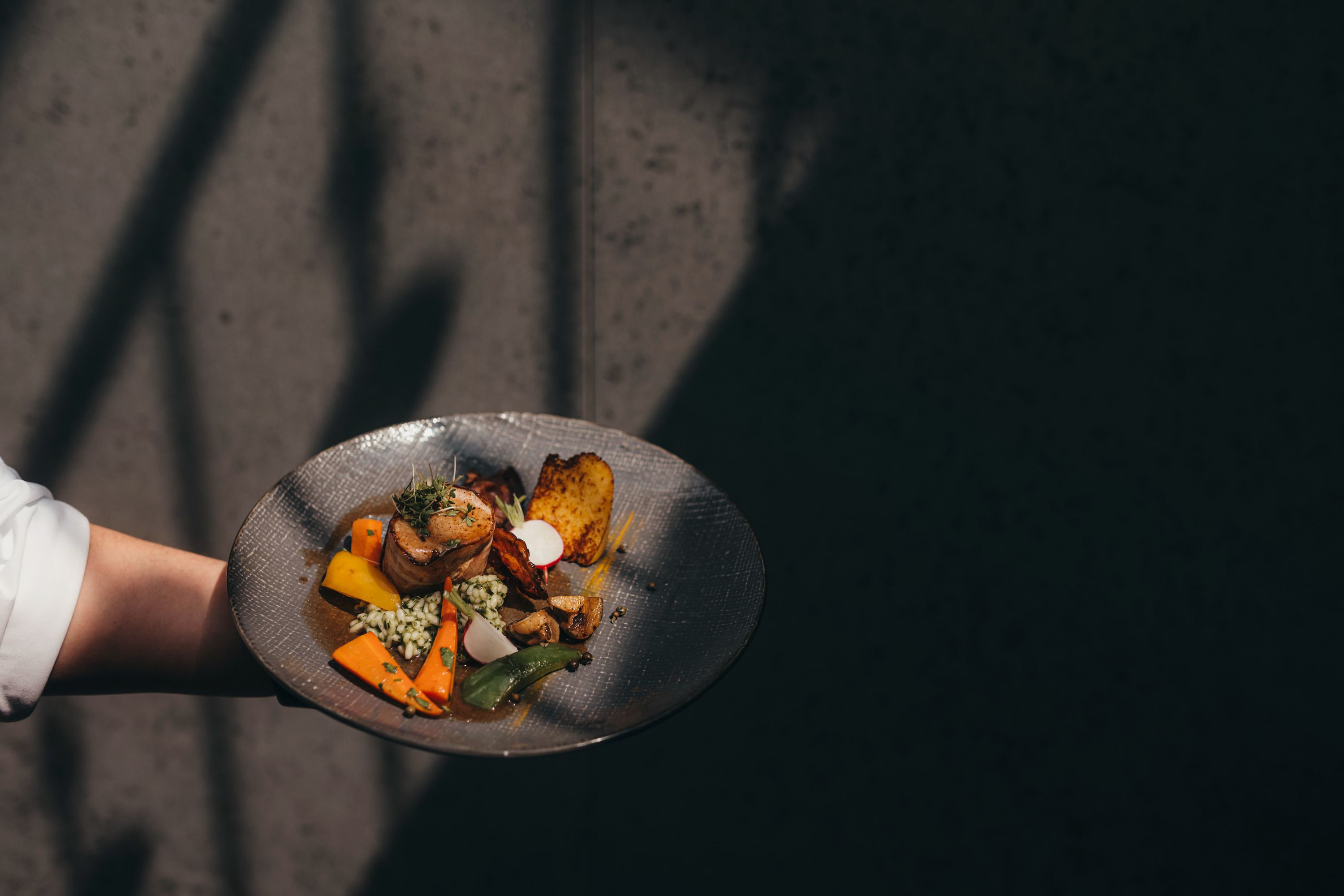 A plate with a modern interpretation of Waldviertel cuisine, presented by one hand against a dark background.