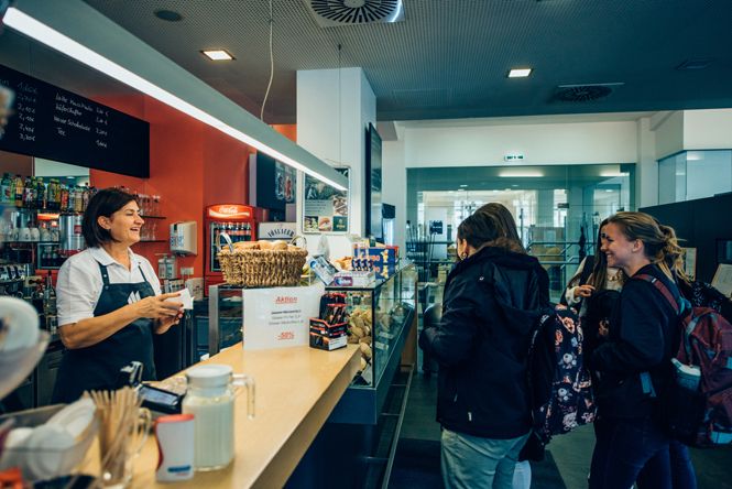 A café employee serves two customers at the counter.