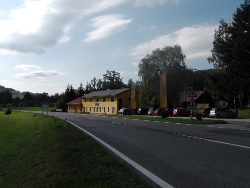 A yellow building on a country road with parked cars and trees in the background.