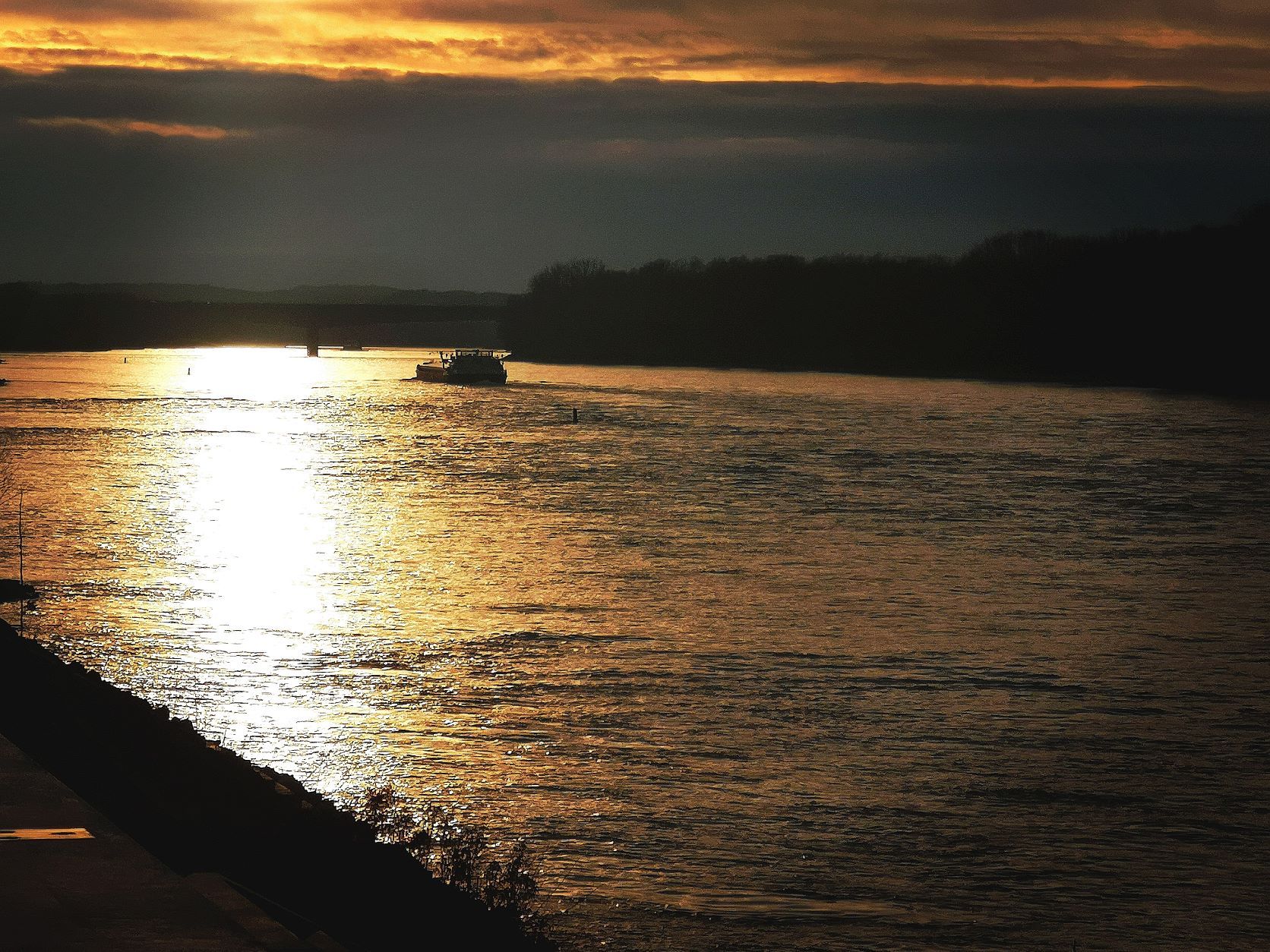 Sunset over a river with a boat and dark clouds in the sky.