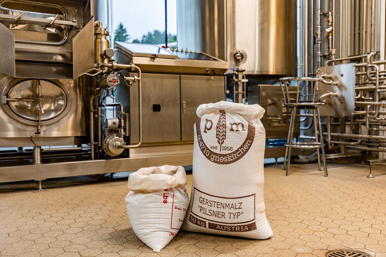 Bags of barley malt in a brewery in front of stainless steel machines.