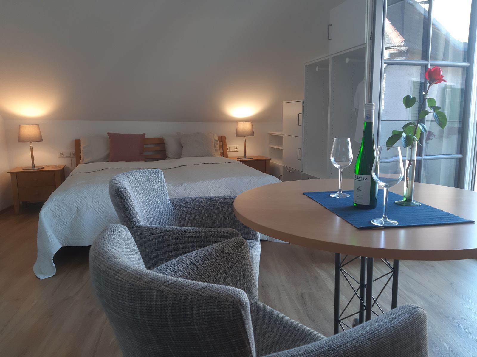 Cozy bedroom with double bed, table, two chairs, wine bottle and glasses.