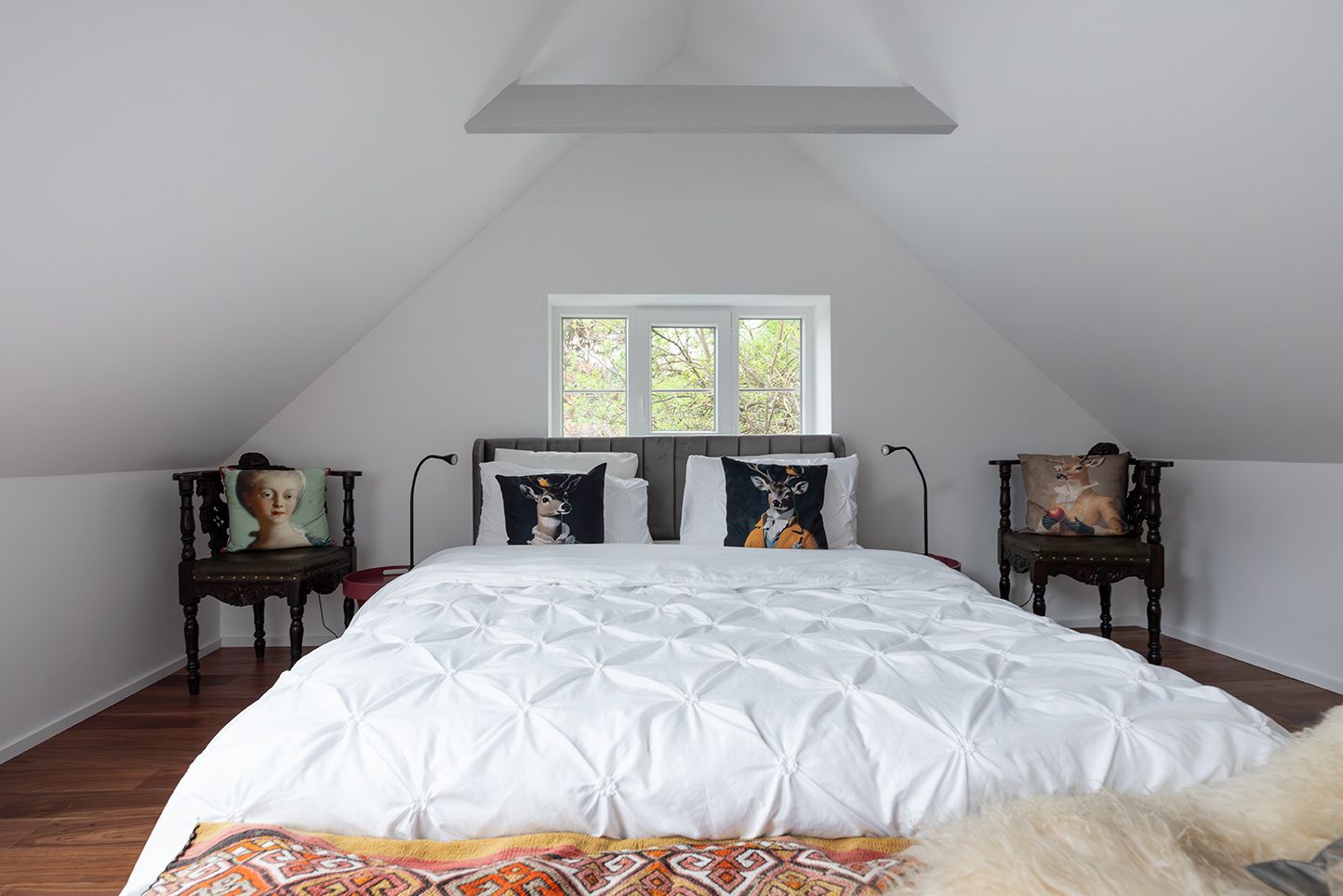 A stylishly furnished bedroom with a large bed, decorative cushions and two antique chairs in an attic room.