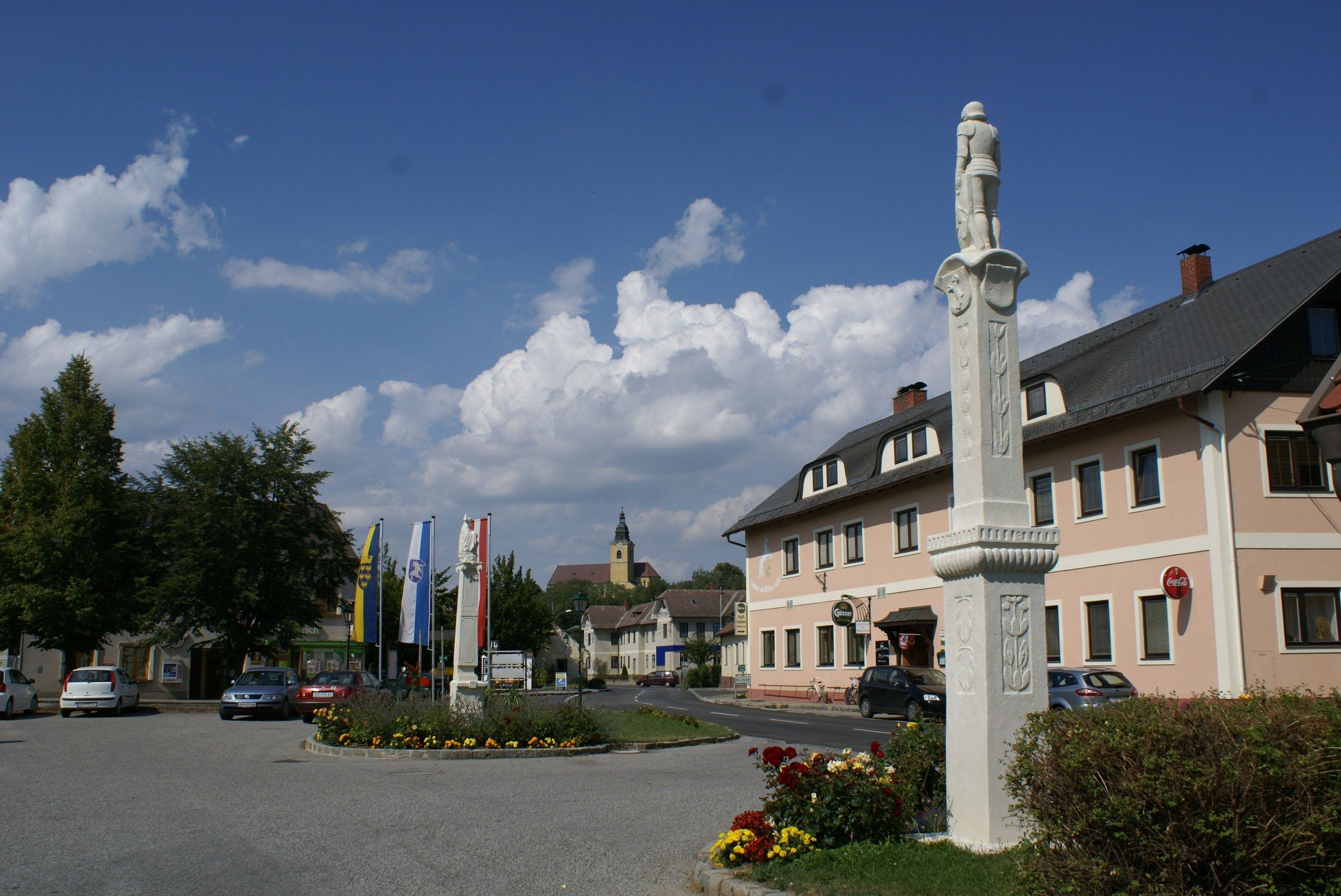 A square in Weitersfeld with a statue, several flags and a building in the background.