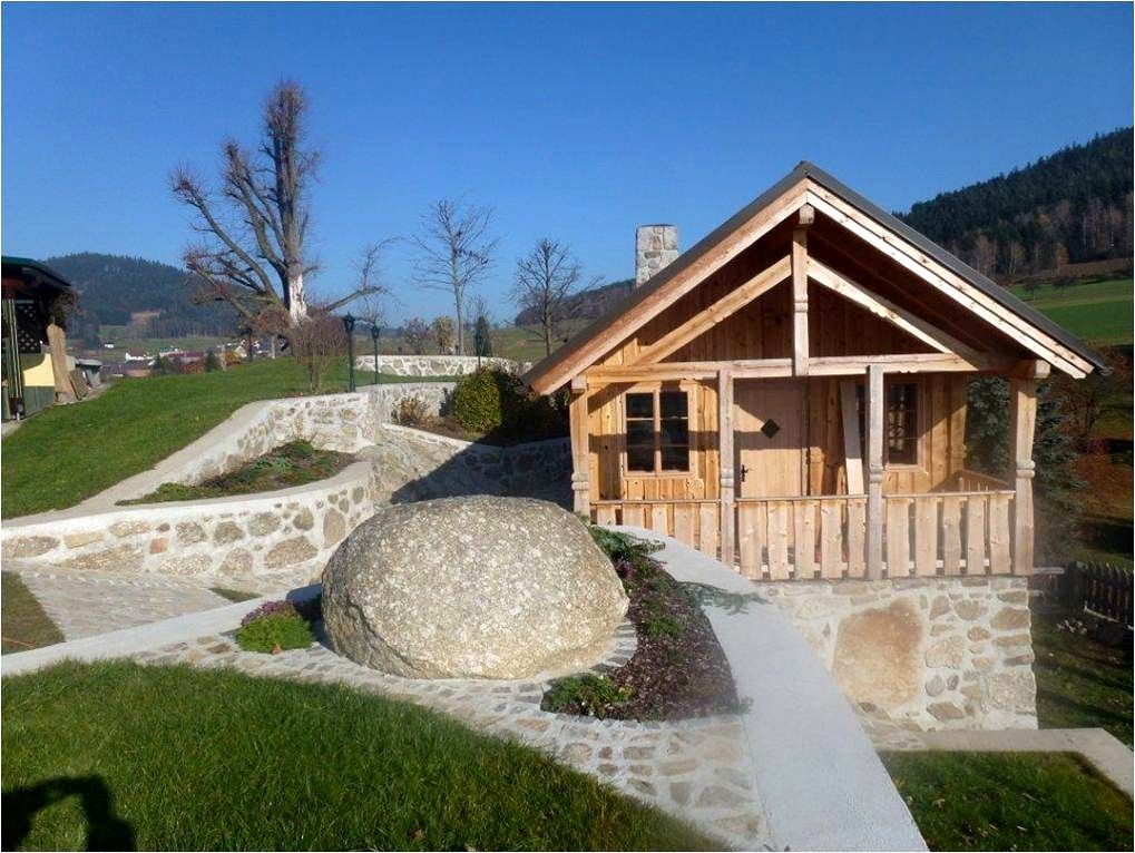 Small wooden house in a garden with stone walls and a large rock.