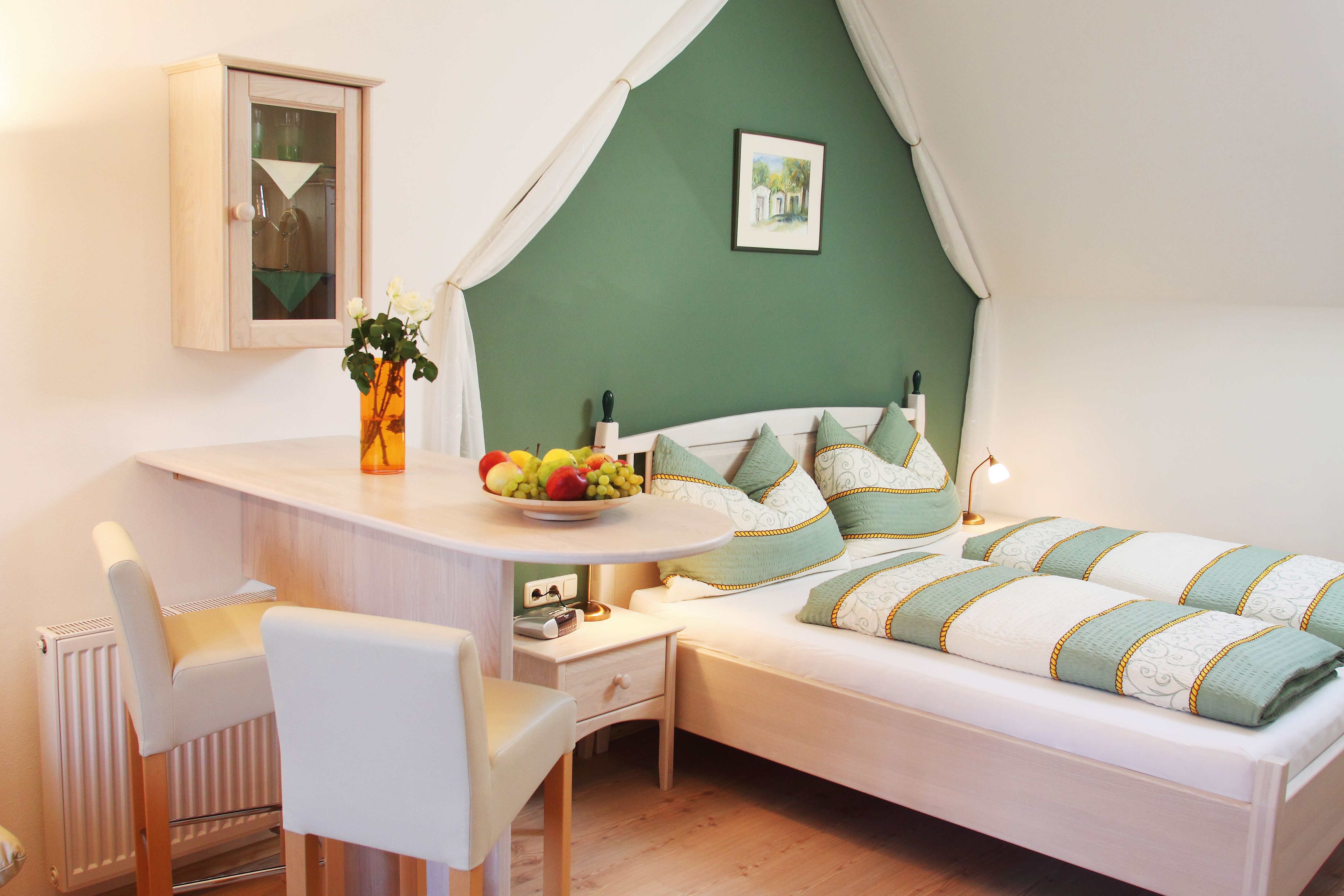 Cozy bedroom with green and white bed linen, wooden furniture and decorations.