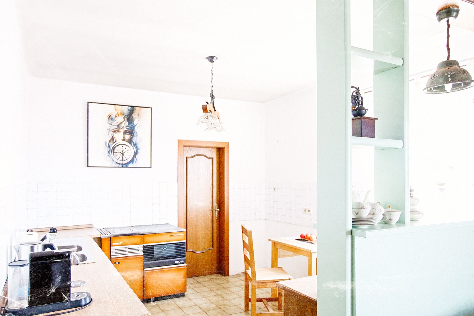 A bright kitchen with wooden furniture, a painting on the wall, and a coffee maker on the countertop.