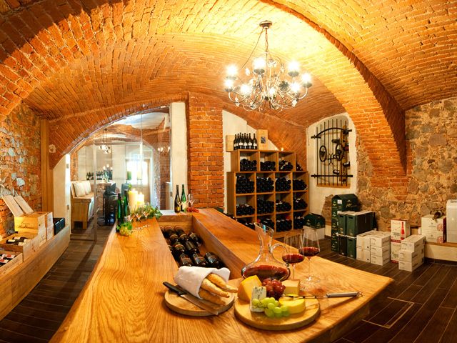 A cozy wine cellar with brick walls, a wooden table, shelves of wine bottles and a plate of cheese and grapes.