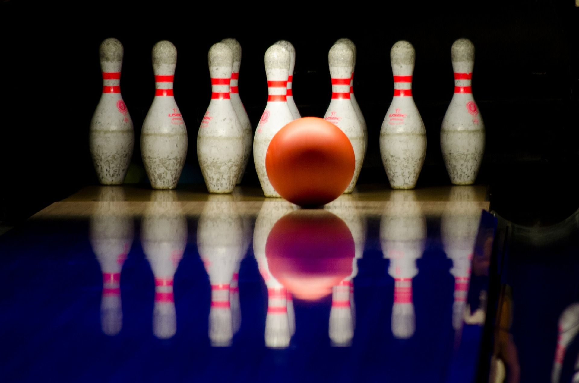 A bowling ball rolls towards a group of pins.