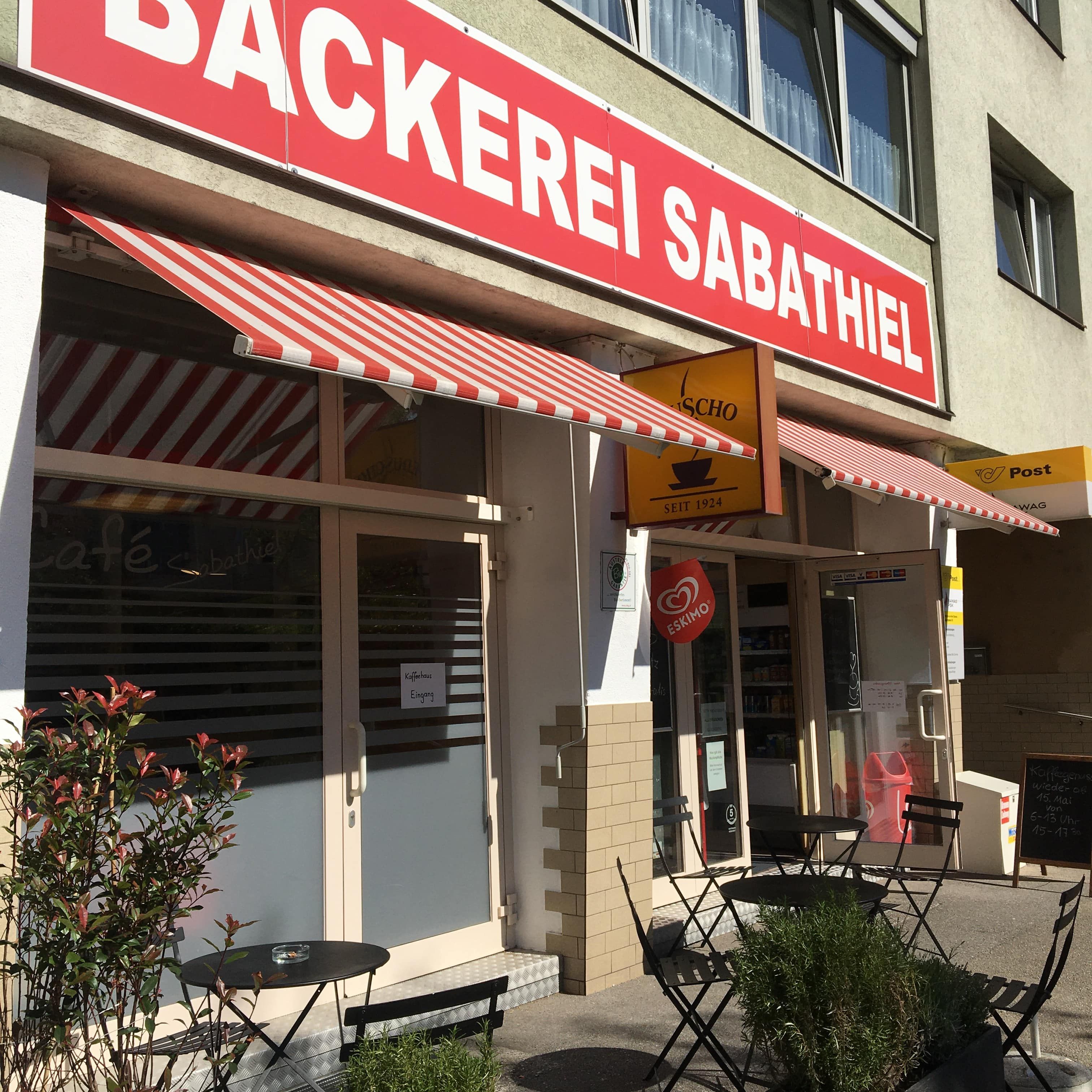 Exterior view of a bakery with red awnings and outdoor seating.