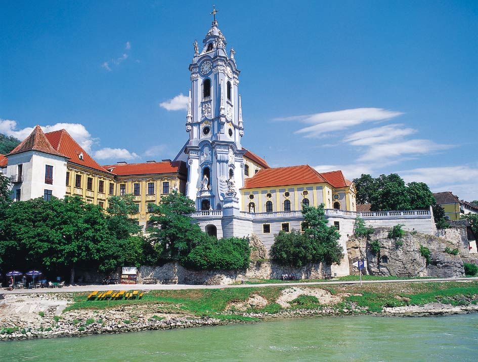 Baroque church with blue and white façade and red roof on a riverbank.