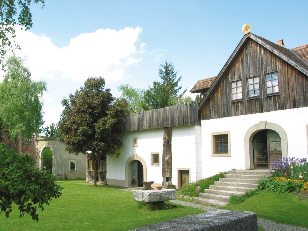A traditional building with a wooden roof and white façade, surrounded by a green garden.