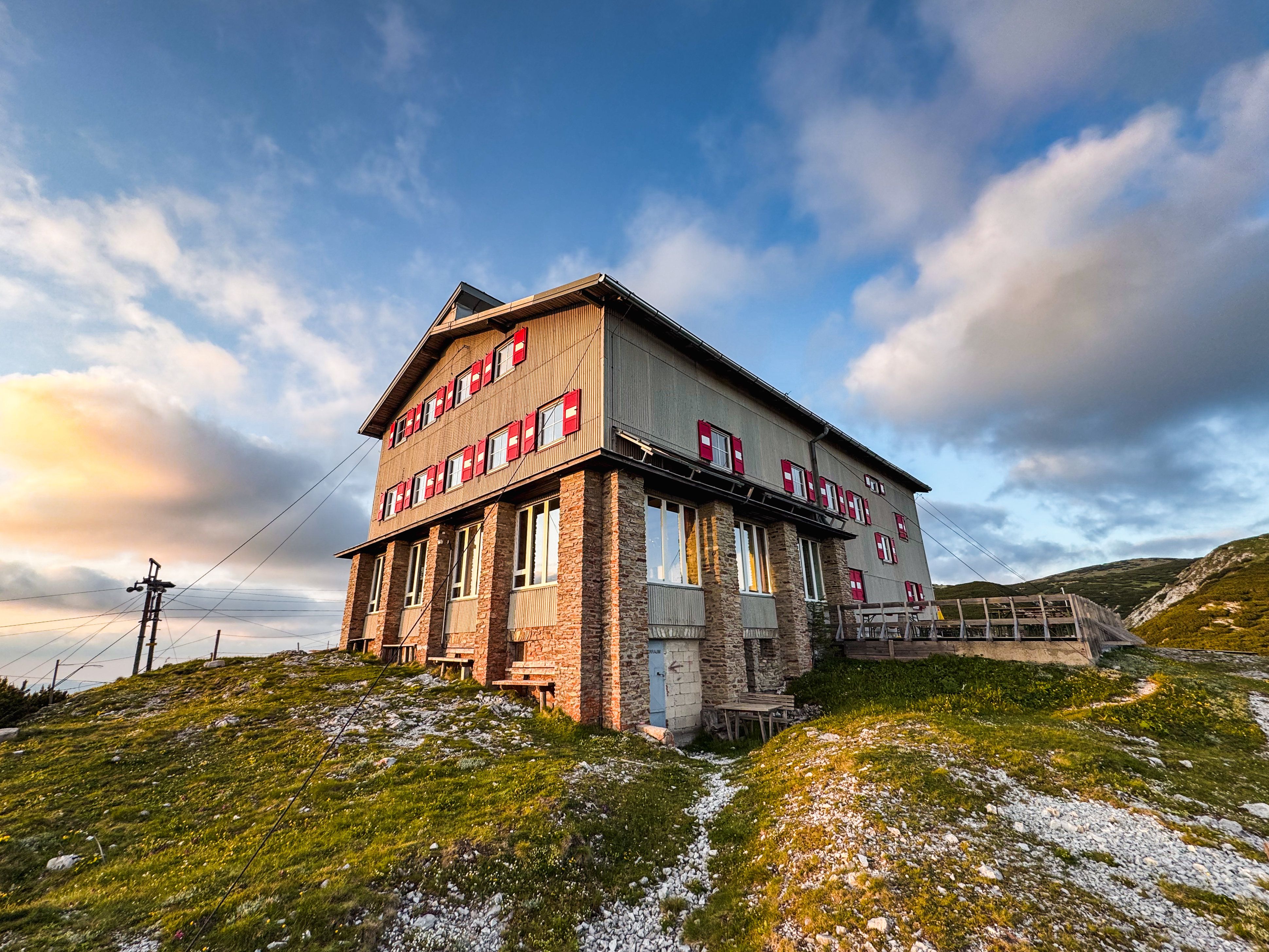 The Habsburghaus on the Raxalpe at sunset, surrounded by green meadows and a clear sky with few clouds.