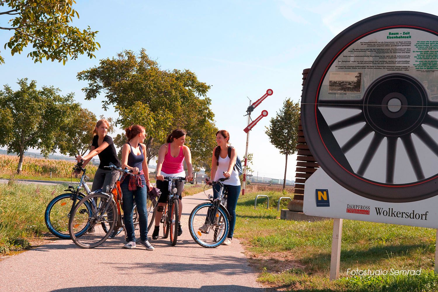 Four women with bicycles on a cycle path next to a large bicycle monument in Wolkersdorf.
