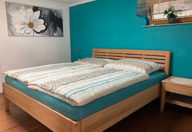 Bedroom with double bed, turquoise wall and flower picture.