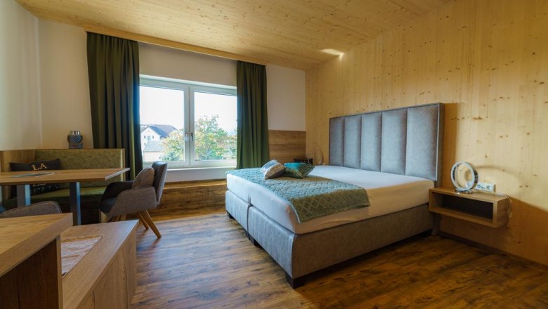 Modern hotel room with double bed, wooden walls and large window.