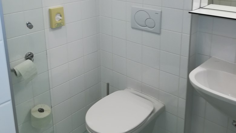 Small bathroom with white tiled walls, a toilet, washbasin and toilet roll holder.