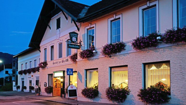 A traditional inn with windows decorated with flowers at dusk.