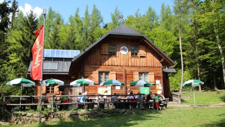 Wooden hut in the forest with sunshades and people on the terrace.