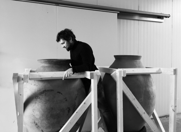 Person next to large clay amphorae in a wine cellar.