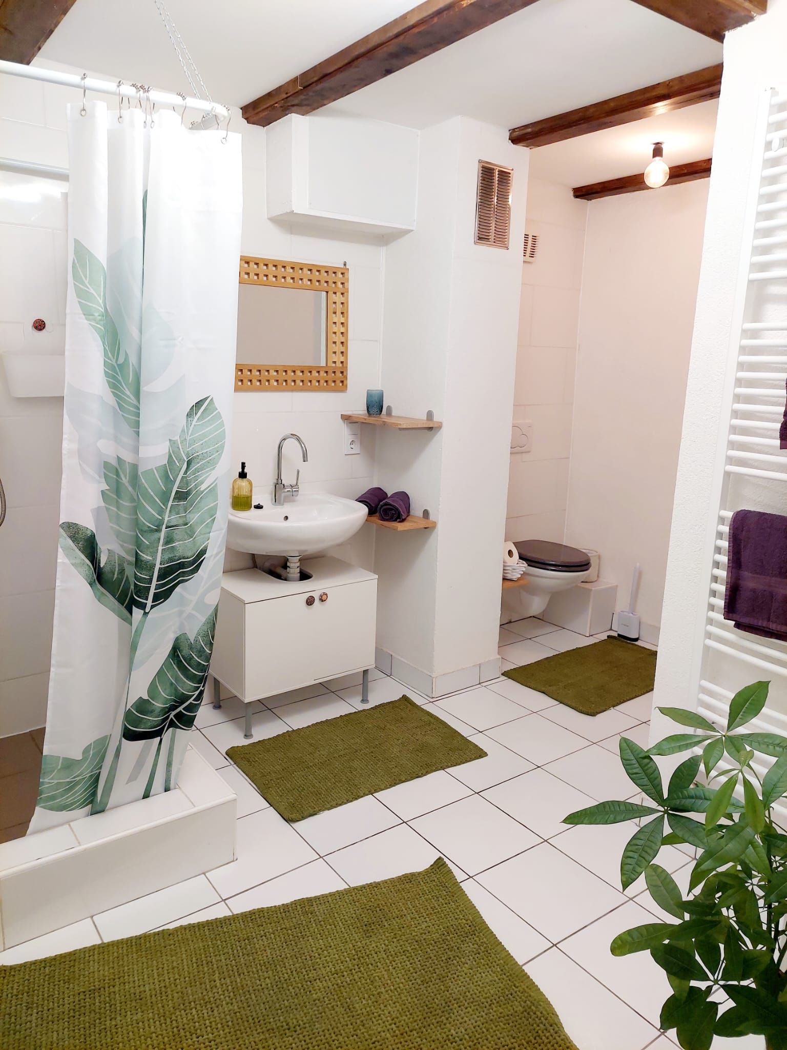 Modern bathroom with white tiles, green carpets and plant motif shower curtain.
