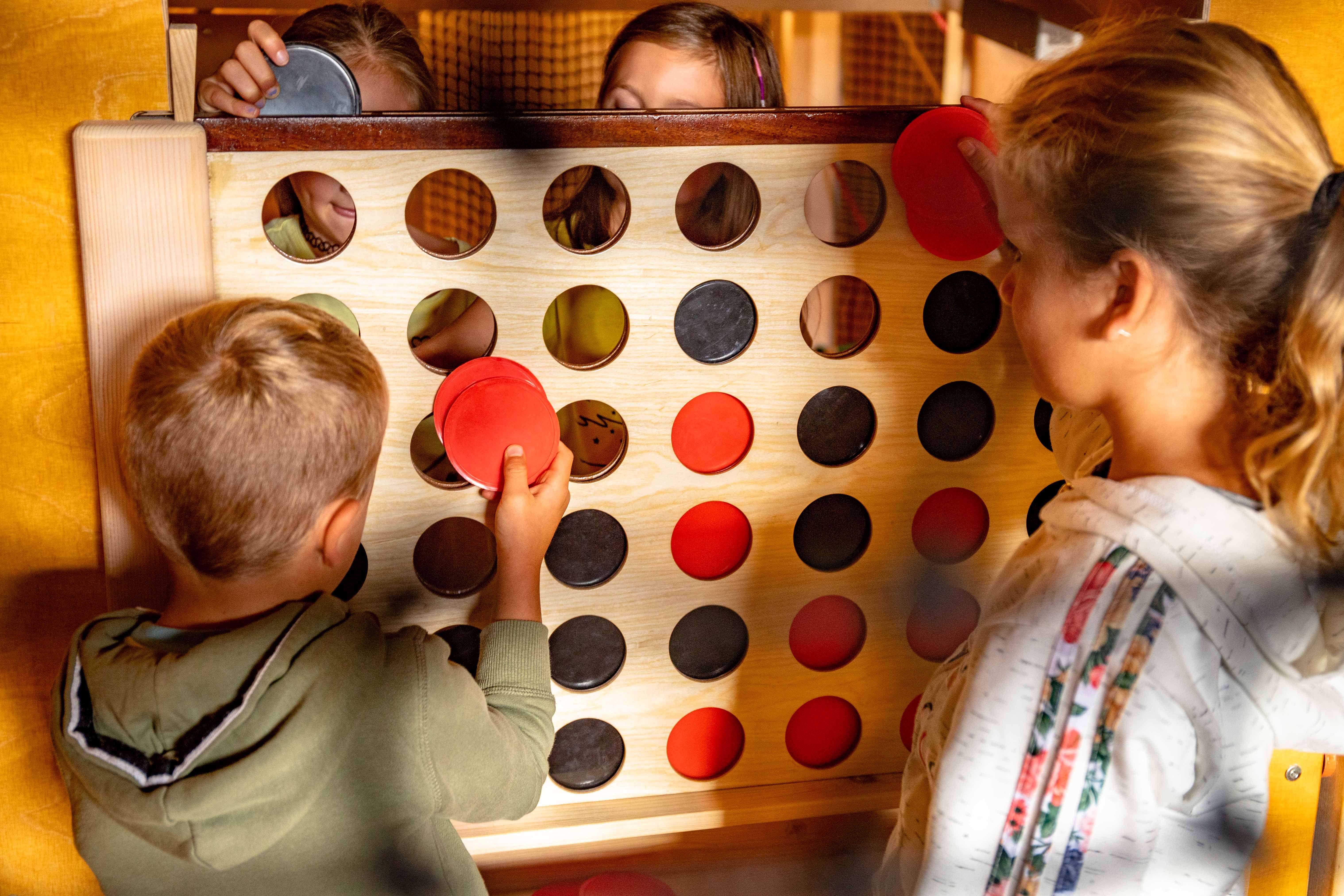 Children play a big four-in-a-row game with red and black disks.