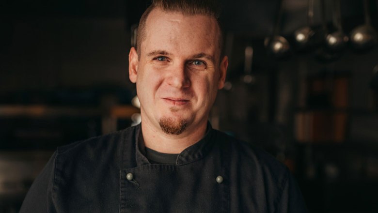 A man in chef's clothes stands in a kitchen.