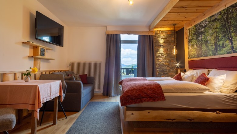 Comfortable hotel room with double bed, sofa, table and large window with mountain view.