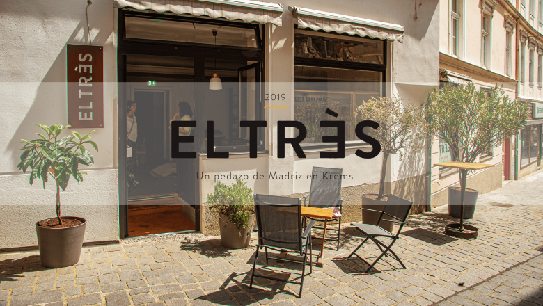 Exterior view of a café called EL TRÈS, seating and plants in front of the entrance.