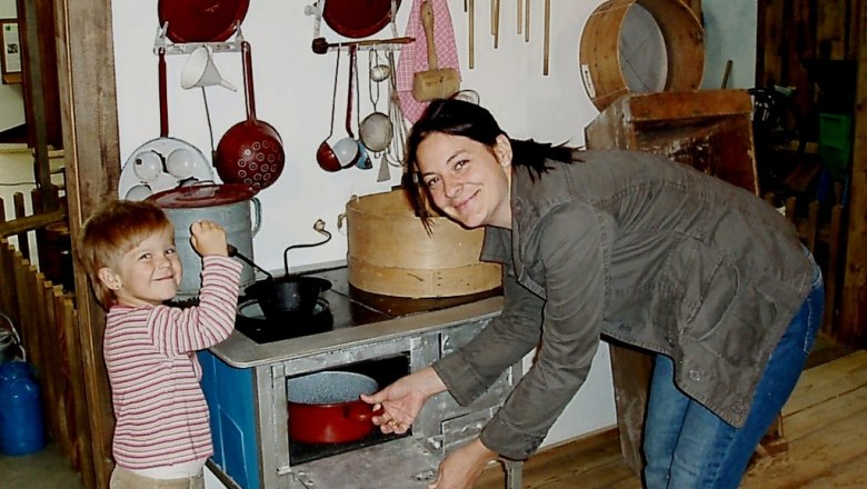 A woman and a child play in a historic kitchen with old kitchen utensils.