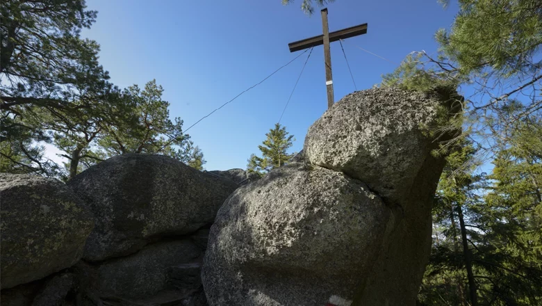 Large rocks with a wooden cross on a wooded hill.