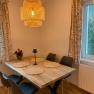 Dining area with wooden table, four black chairs, round lamp and window with curtains.