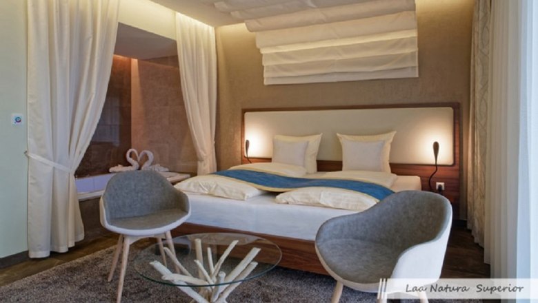 Modern double room with large bed, two gray chairs and a glass table.