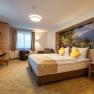 Modern hotel room with double bed, yellow pillows, desk, armchair and large window.