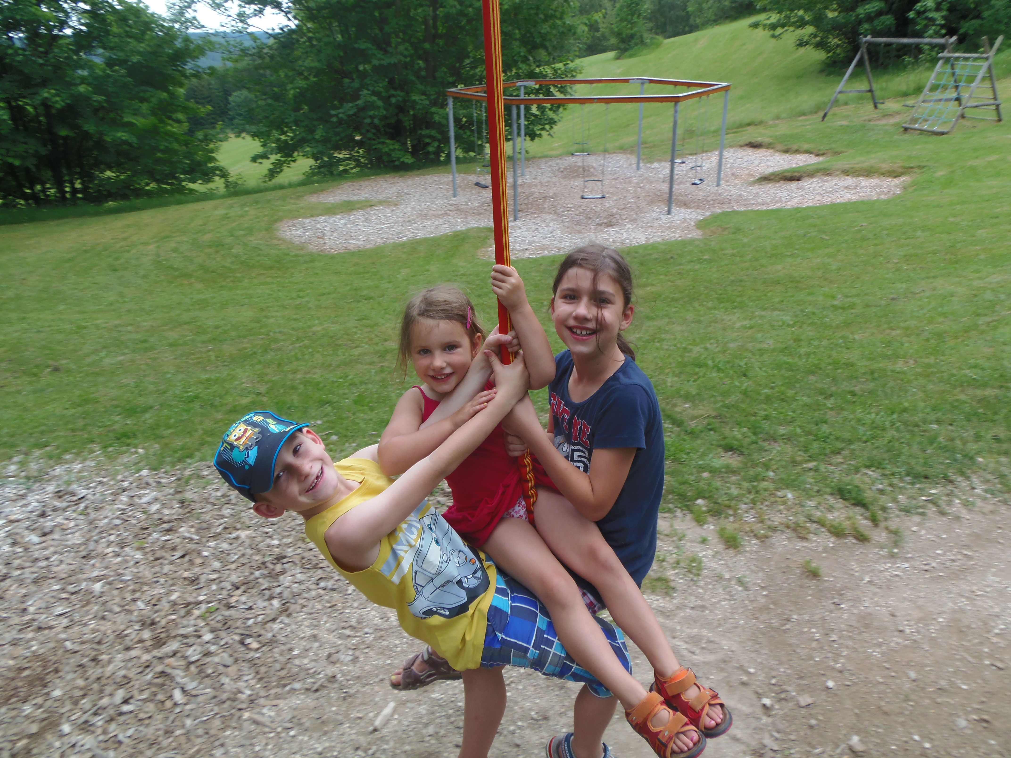 Three children swinging happily on a ropeway in a playground.