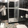 Modern bathroom with black tiled wall, colorful floor tiles, shower, towel and toilet.